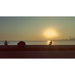 Silhouette people on sea against clear sky during sunset