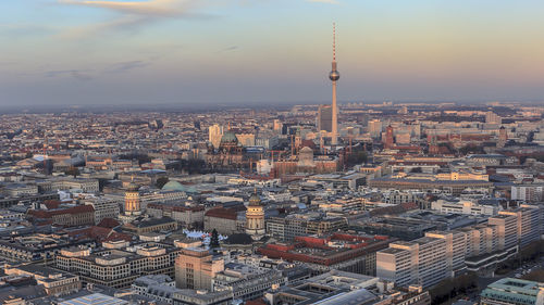 Fernsehturm amidst cityscape against sky during sunset