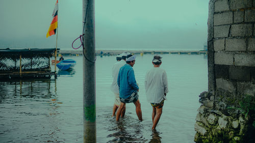 Rear view of men standing at beach against sky