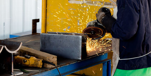 Midsection of manual worker working on metal structure in factory