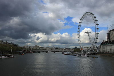 Ferris wheel in city against cloudy sky