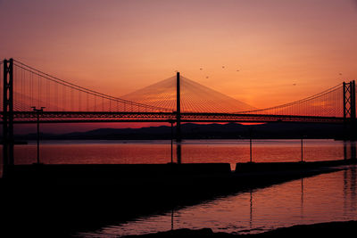 Silhouette bridge over sea against sky during sunset