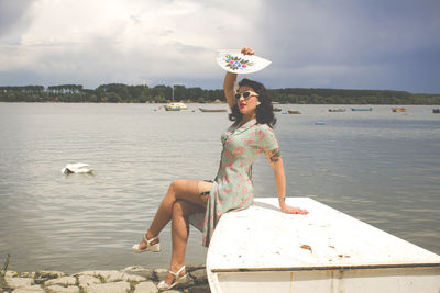 Pinup woman sitting by lake against sky