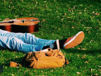 Low section of man by lying by guitar and bag at park