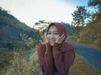 Portrait of smiling young woman standing against trees