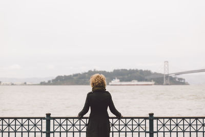 Rear view of woman standing by railing on pier over sea against sky