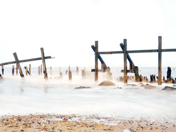 Wooden posts on beach against clear sky