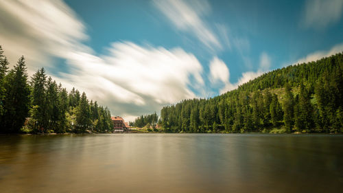 Lake with trees and house against cloudy sky