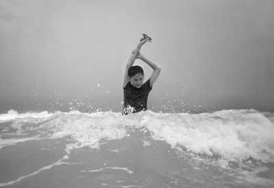 Full length of man splashing water in sea against sky