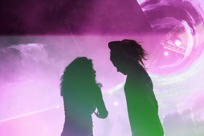 Low angle view of silhouette woman dancing against purple at night