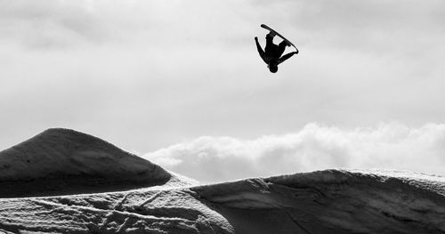 Low angle view of man jumping on mountain against sky