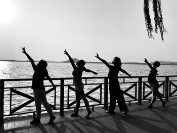 Silhouette people dancing on pier over sea against sky