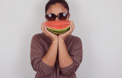 Portrait of woman wearing sunglasses holding melon against wall