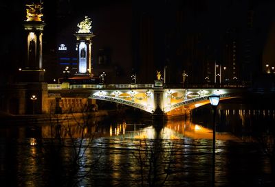 Illuminated bridge over river in city at night