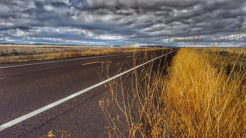 Road amidst field against storm clouds