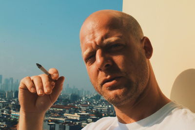 Close-up portrait of man smoking cigarette with cityscape in background