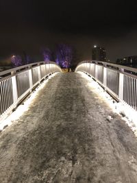 Illuminated footbridge in city against sky at night