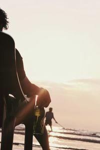 Rear view of man on beach against sky during sunset