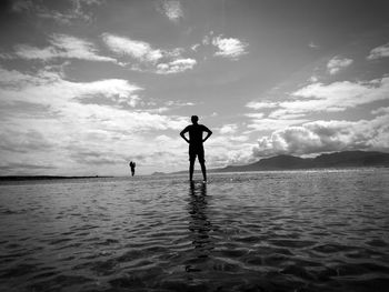 Rear view of silhouette men standing in sea against sky