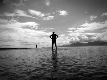 Rear view of silhouette man standing in sea against sky