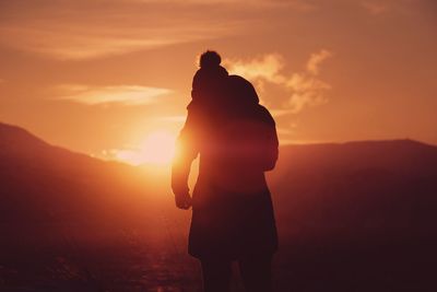Rear view of silhouette man standing against orange sky