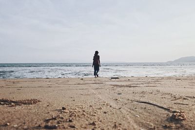 Rear view of woman on beach against sky