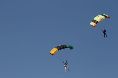 Low angle view of men paragliding against clear sky
