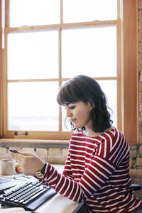 Businesswoman using smart phone while sitting at desk in office