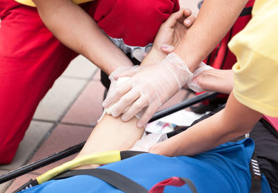 Cropped hands of people bandaging man indoors