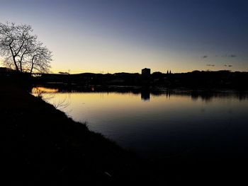 Silhouette trees by lake against sky during sunset