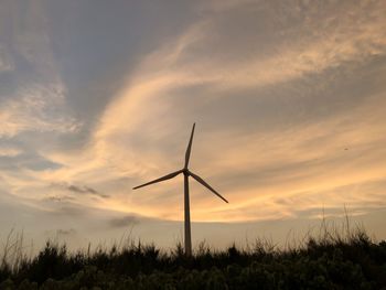 Wind turbines on field against sky during sunset