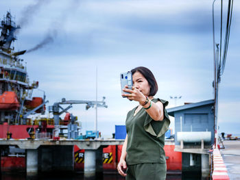 Young woman using phone while standing against sky