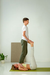 A guy in sportswear is doing yoga, standing on his hands, a slender woman lying on a sports mat.