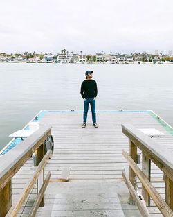 Man standing on jetty over lake against sky