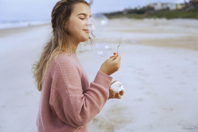 Portrait of teenage girl blowing soap bubbles on beach