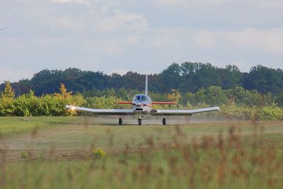 Airplane flying over grass against sky