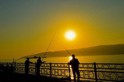 Silhouette people fishing by sea against sky during sunset