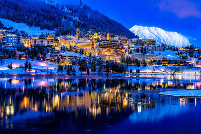 Illuminated buildings by lake against sky at night