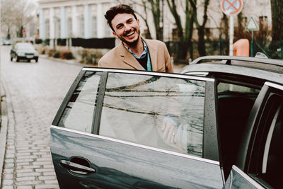 Portrait of smiling young man entering in car on street