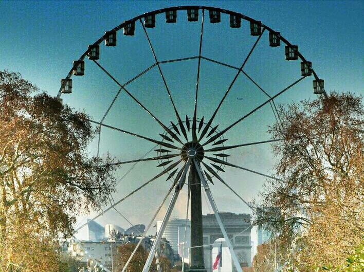 ferris wheel, amusement park, amusement park ride, low angle view, arts culture and entertainment, built structure, architecture, sky, building exterior, circle, clear sky, day, fun, metal, blue, outdoors, fairground ride, large, tree, geometric shape