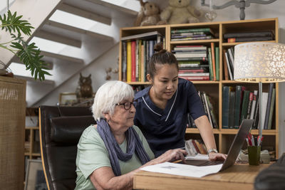 Home carer helping senior woman to use laptop