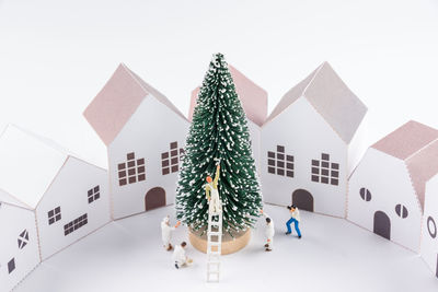 Close-up of figurines with christmas tree and model homes against white background