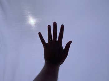 Close-up of hand touching silhouette against blue sky