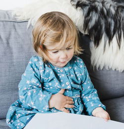 Cute girl with book sitting on sofa at home