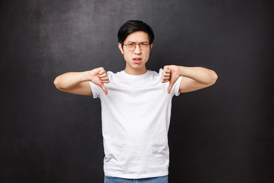 Man showing thumbs down gesture against black background