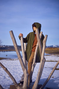 Young man looking away while standing by wooden posts against sky