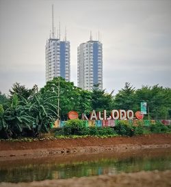 Information sign by trees and buildings against sky