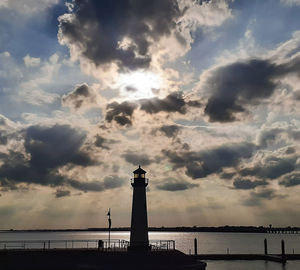 Lighthouse by sea against sky during sunset