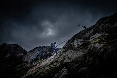 Low angle view of people on rock against sky