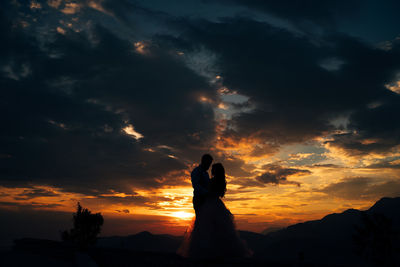 Silhouette couple standing against orange sky